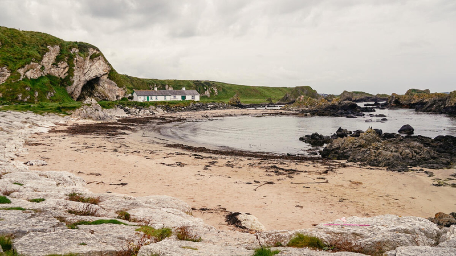A whitewashed fisherman’s cottage on the beach at Ballintoy Harbour, beside a rock arch