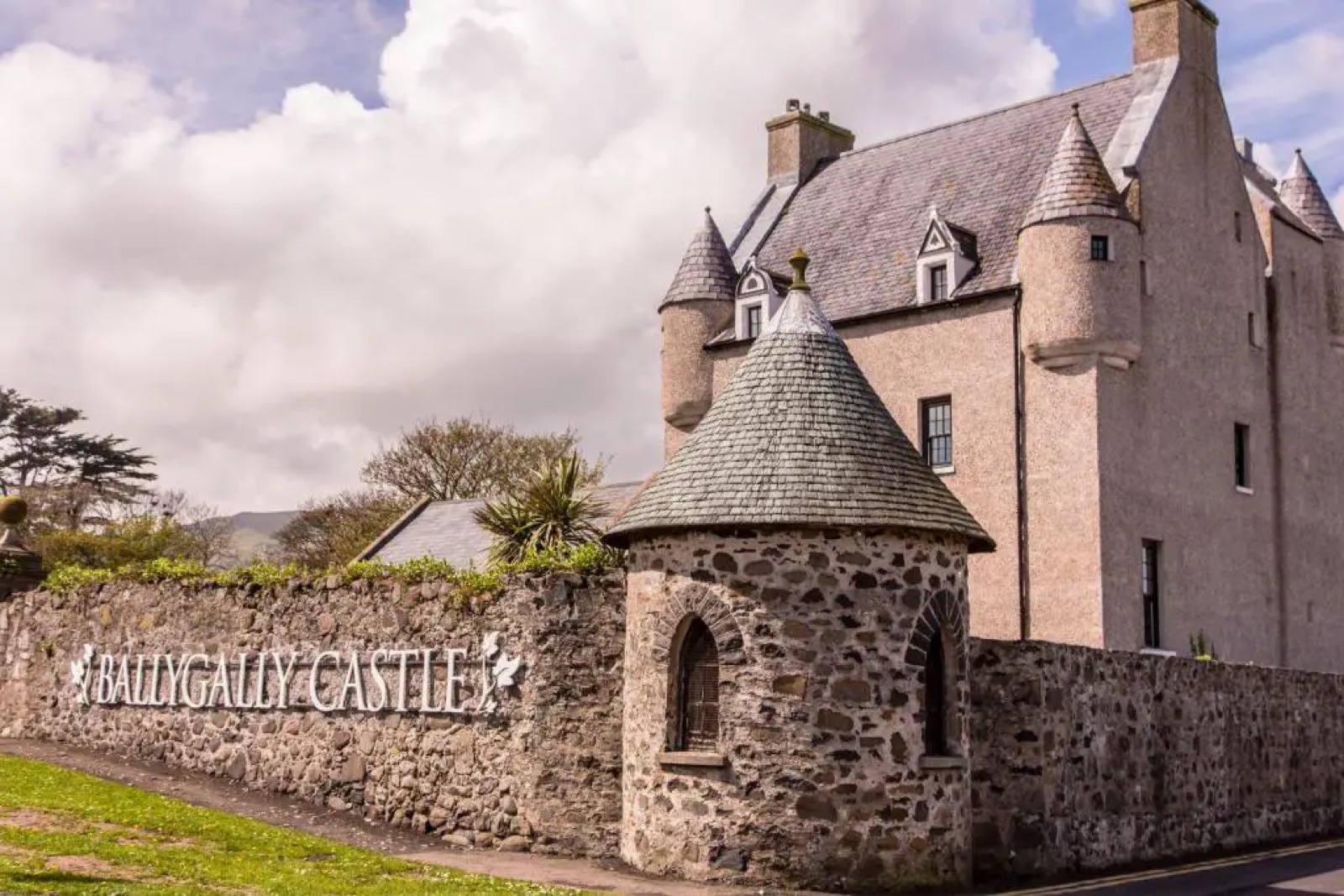 The pink-washed Ballygally Castle building with its stone gatehouse and turret entrance sign