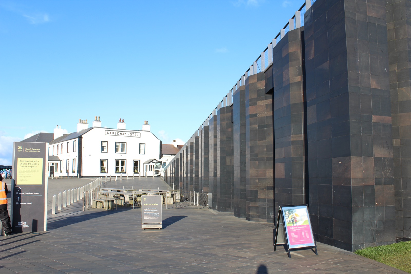 The Causeway Hotel and the dark basalt-column-inspired Visitor Centre building side by side under a blue sky