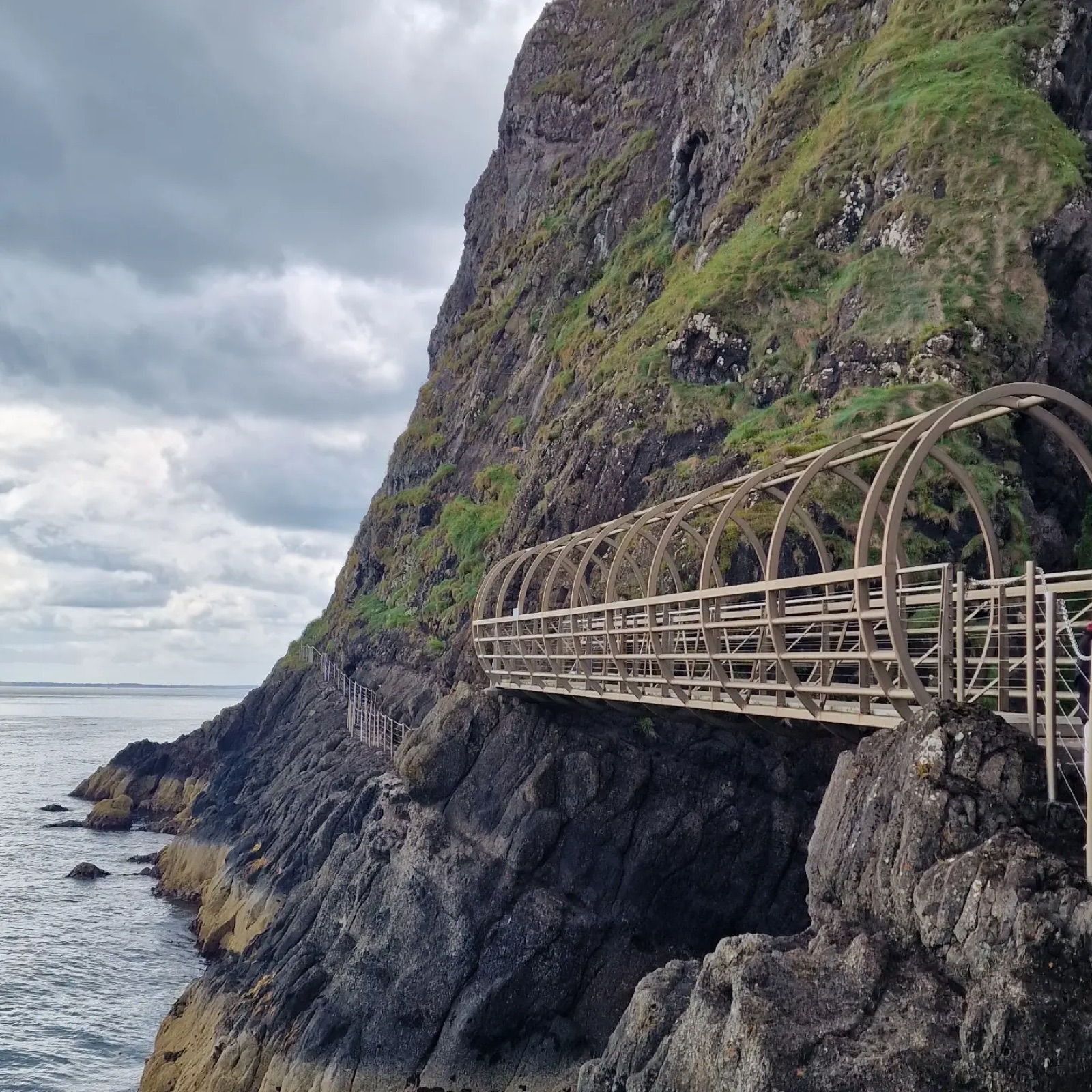 A curved metal bridge from The Gobbins cliff path bolted onto the rock face above the sea