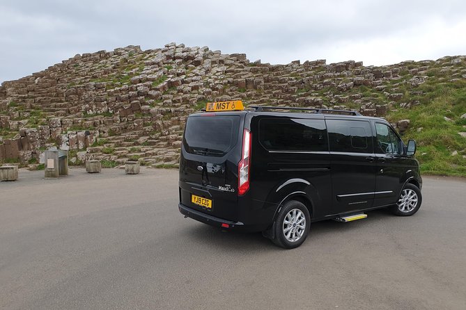 A black taxi tour vehicle parked in front of the Giant’s Causeway basalt columns