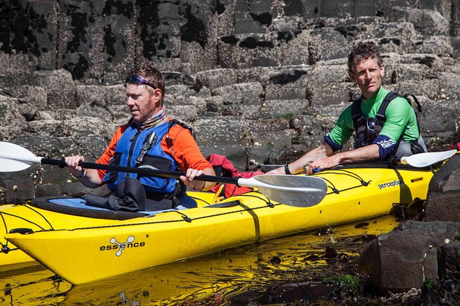Two kayakers paddling a yellow tandem kayak past the basalt columns